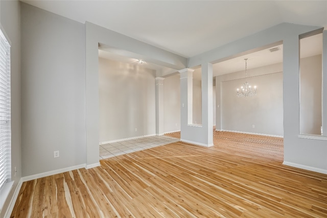 empty room with an inviting chandelier, ornate columns, and light hardwood / wood-style flooring