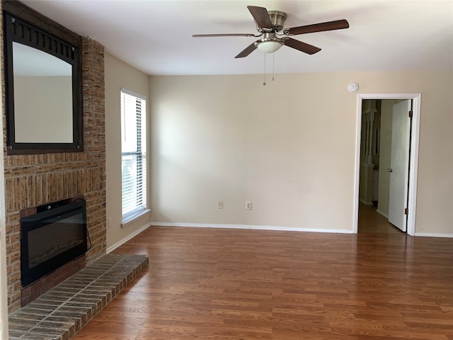 unfurnished living room featuring dark hardwood / wood-style flooring, ceiling fan, and a brick fireplace