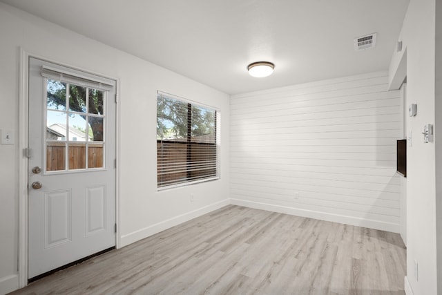 entryway with light wood-type flooring, wooden walls, and a healthy amount of sunlight