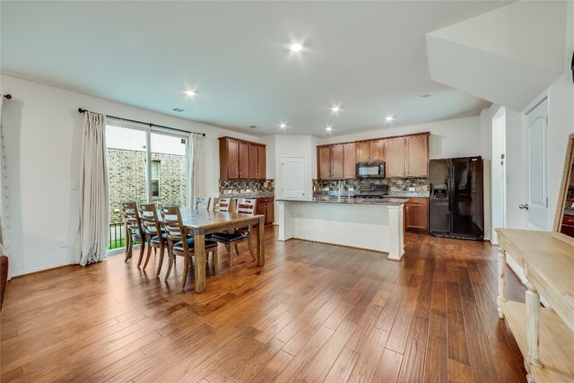 kitchen with hardwood / wood-style floors, black appliances, and a center island with sink