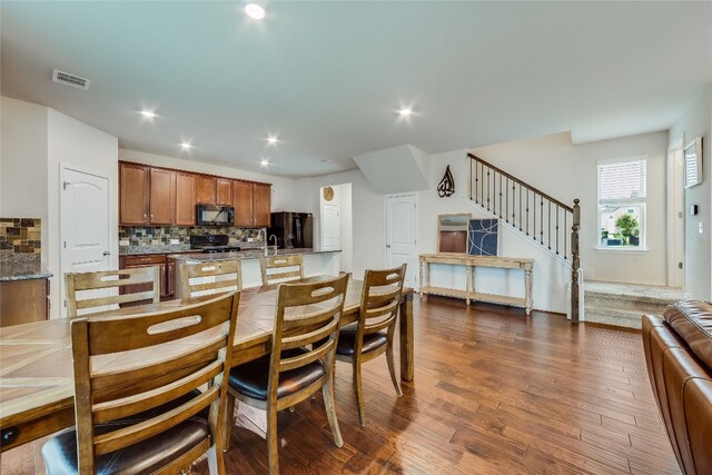 kitchen featuring light stone counters, black appliances, hardwood / wood-style flooring, sink, and backsplash