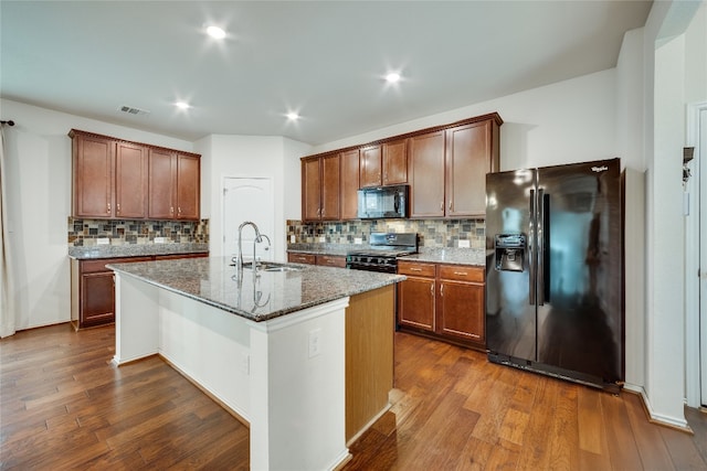 kitchen featuring black appliances, a center island with sink, dark hardwood / wood-style floors, and dark stone countertops