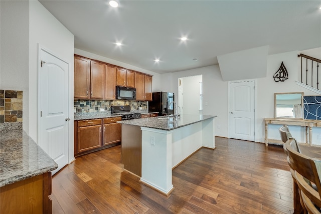 kitchen with stone countertops, a center island with sink, black appliances, backsplash, and dark hardwood / wood-style flooring