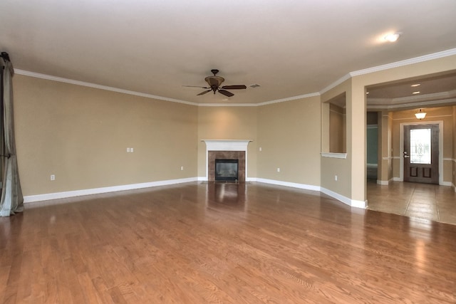 unfurnished living room with a tiled fireplace, wood-type flooring, ceiling fan, and ornamental molding