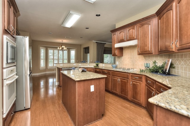 kitchen with an inviting chandelier, kitchen peninsula, a kitchen island, light stone countertops, and light hardwood / wood-style flooring