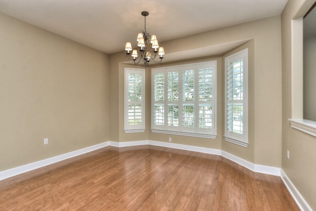 empty room with hardwood / wood-style flooring and an inviting chandelier