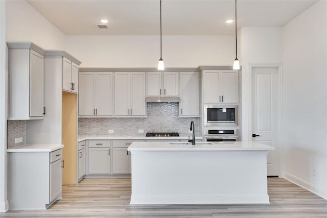 kitchen featuring under cabinet range hood, stainless steel appliances, light countertops, and a sink