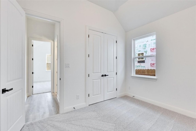 unfurnished bedroom featuring baseboards, light carpet, a closet, and vaulted ceiling