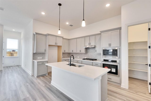kitchen with gray cabinetry, a sink, under cabinet range hood, appliances with stainless steel finishes, and light countertops