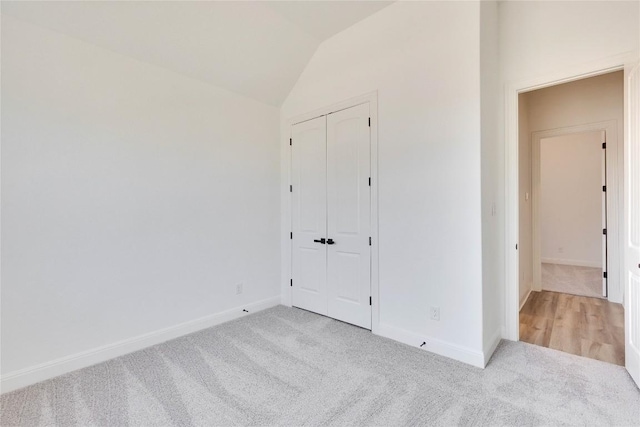 unfurnished bedroom with vaulted ceiling, baseboards, a closet, and light carpet