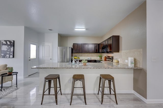 kitchen with a kitchen bar, kitchen peninsula, appliances with stainless steel finishes, and dark brown cabinets