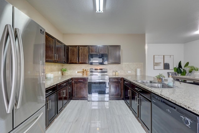 kitchen featuring stainless steel appliances, sink, light stone counters, tasteful backsplash, and dark brown cabinets