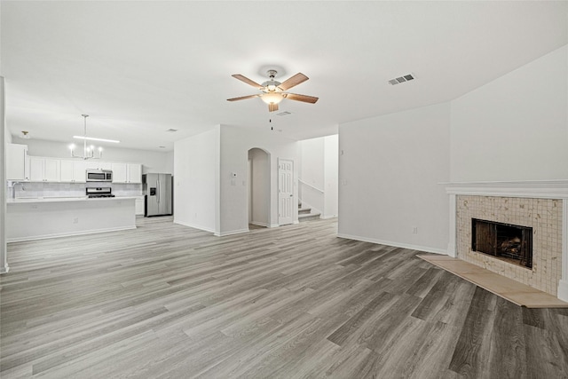 unfurnished living room with ceiling fan with notable chandelier, light hardwood / wood-style floors, sink, and a tiled fireplace