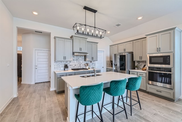 kitchen with gray cabinets, an island with sink, sink, a kitchen breakfast bar, and stainless steel appliances