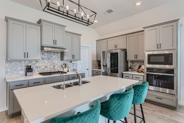 kitchen featuring appliances with stainless steel finishes, a kitchen bar, sink, and a center island with sink