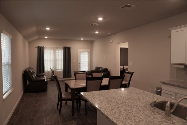 kitchen with dark wood-type flooring, light stone countertops, vaulted ceiling, and white cabinets