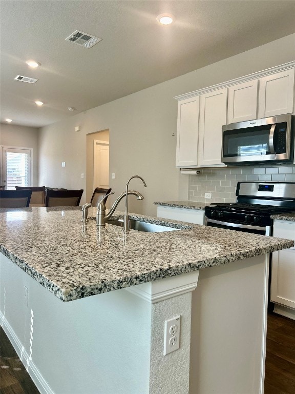 kitchen featuring stainless steel appliances, dark hardwood / wood-style flooring, a center island with sink, and white cabinets