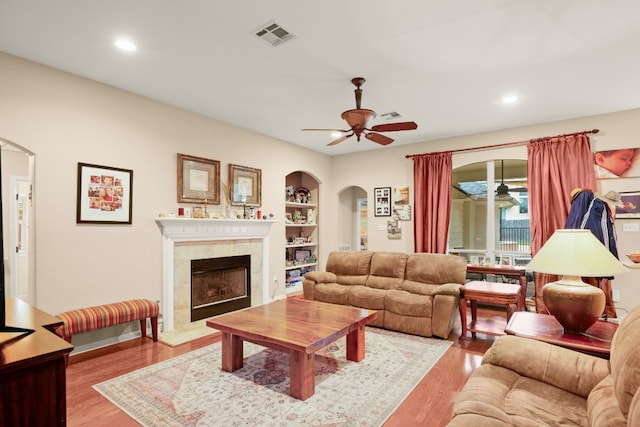 living room with light hardwood / wood-style floors, ceiling fan, a tile fireplace, and built in features