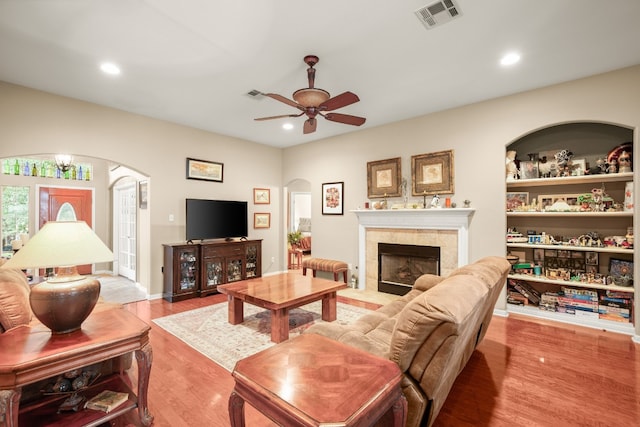 living room with ceiling fan, a tile fireplace, and light wood-type flooring