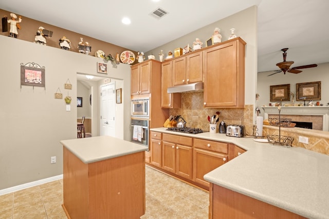 kitchen with stainless steel appliances, a kitchen island, kitchen peninsula, a tile fireplace, and ceiling fan