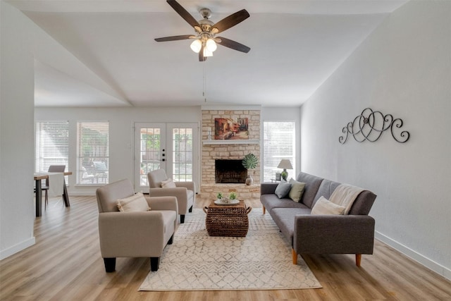 living room with lofted ceiling, french doors, a stone fireplace, ceiling fan, and light wood-type flooring