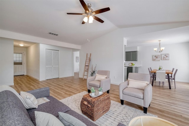 living room with ceiling fan with notable chandelier, lofted ceiling, and light hardwood / wood-style flooring