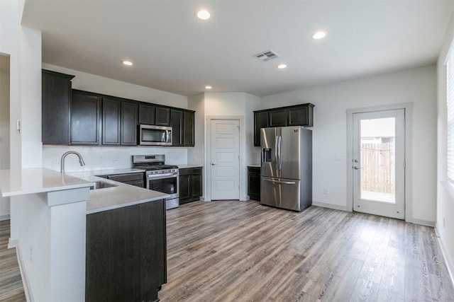 kitchen with kitchen peninsula, tasteful backsplash, stainless steel appliances, sink, and light hardwood / wood-style flooring