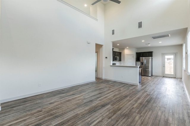 unfurnished living room with a towering ceiling, ceiling fan, and dark wood-type flooring