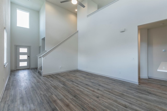 unfurnished living room with ceiling fan, a towering ceiling, and dark hardwood / wood-style floors