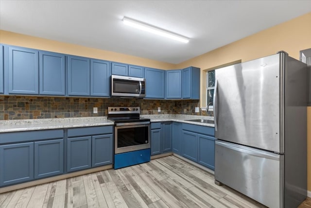 kitchen featuring stainless steel appliances, backsplash, light wood-type flooring, blue cabinetry, and sink