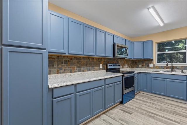 kitchen with backsplash, light wood-type flooring, appliances with stainless steel finishes, blue cabinetry, and sink