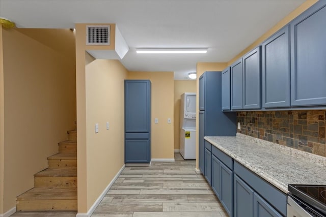 kitchen with tasteful backsplash, light hardwood / wood-style flooring, stacked washer / drying machine, and blue cabinets