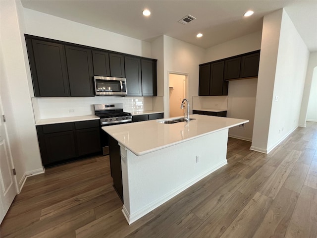 kitchen with stainless steel appliances, hardwood / wood-style flooring, sink, and an island with sink