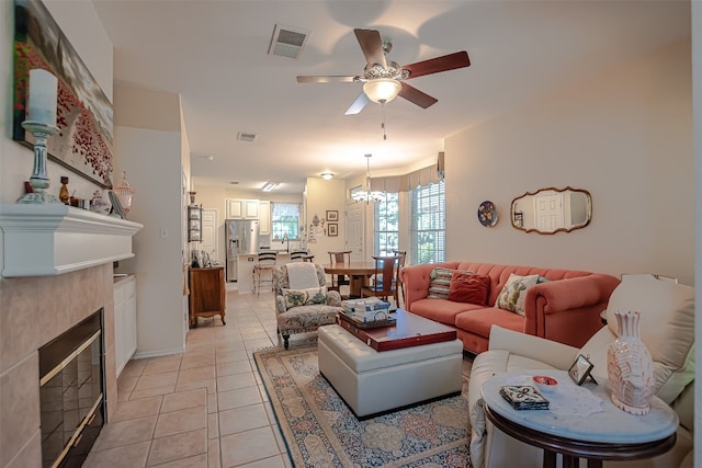 living room featuring light tile patterned flooring, ceiling fan with notable chandelier, and a tiled fireplace