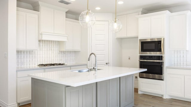 kitchen featuring stainless steel appliances, a sink, visible vents, custom exhaust hood, and light wood finished floors