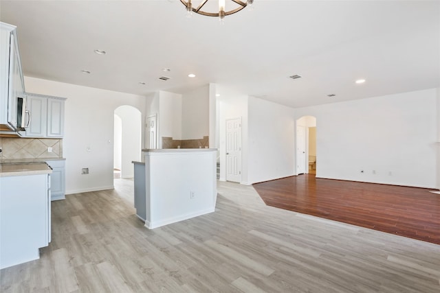 kitchen with a kitchen island, light wood-type flooring, an inviting chandelier, and backsplash