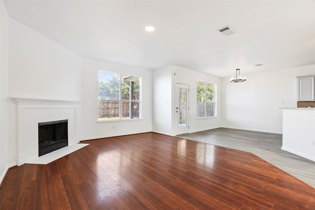 unfurnished living room with dark wood-type flooring, a chandelier, and a tile fireplace