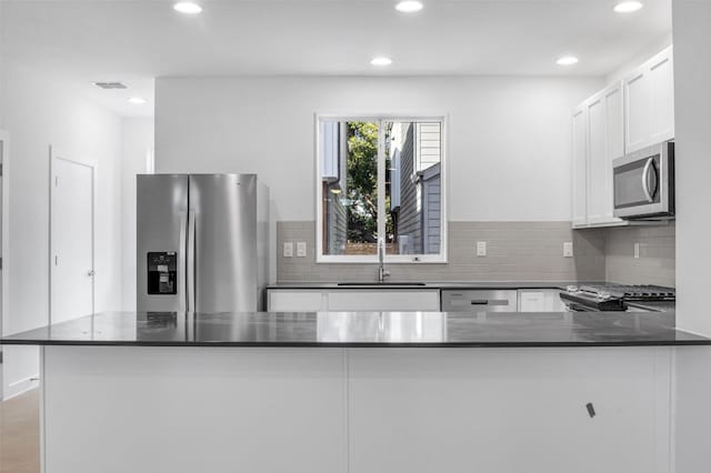 kitchen with sink, kitchen peninsula, appliances with stainless steel finishes, backsplash, and white cabinets