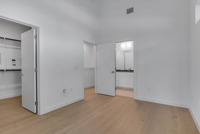 unfurnished bedroom with a closet, a walk in closet, connected bathroom, sink, and light hardwood / wood-style flooring