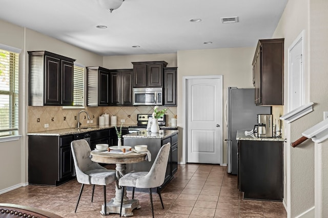 kitchen featuring light stone countertops, appliances with stainless steel finishes, decorative backsplash, and dark brown cabinetry