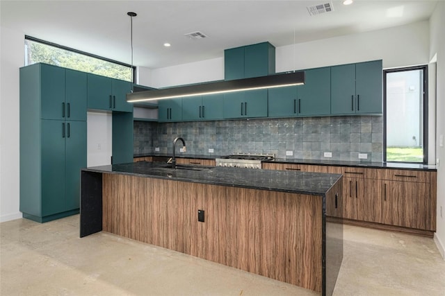 kitchen with dark stone counters, hanging light fixtures, an island with sink, and plenty of natural light