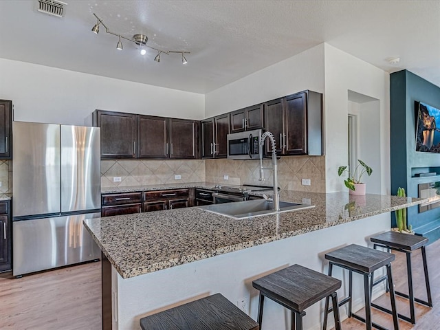 kitchen with kitchen peninsula, stainless steel appliances, a breakfast bar area, and light hardwood / wood-style floors