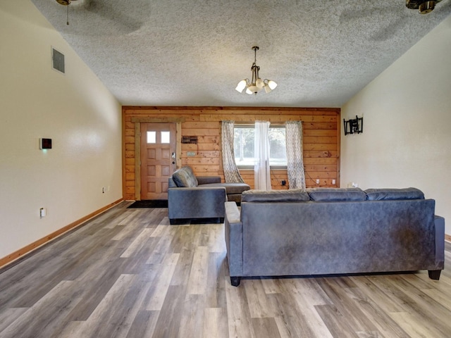 living room with a chandelier, hardwood / wood-style floors, a textured ceiling, and wooden walls