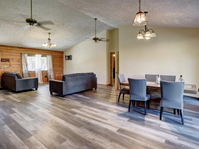 dining space featuring ceiling fan with notable chandelier, a textured ceiling, vaulted ceiling, wooden walls, and hardwood / wood-style floors