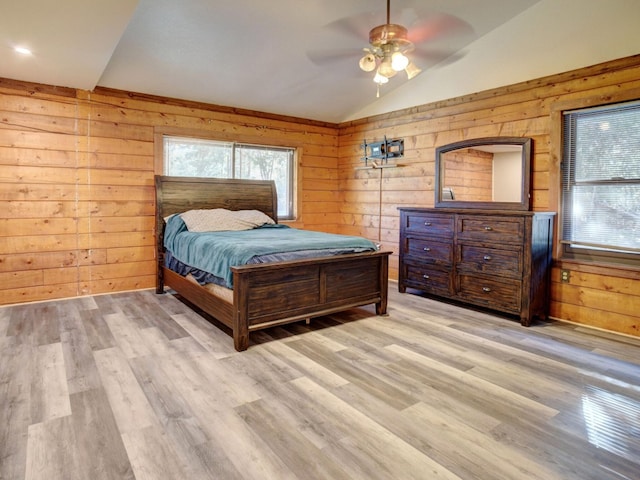 bedroom featuring wood walls, vaulted ceiling, ceiling fan, and light wood-type flooring