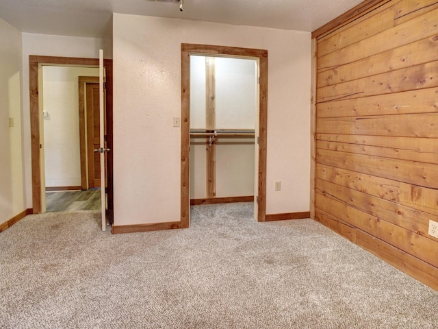 unfurnished bedroom with light carpet, a closet, and wooden walls