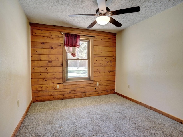 carpeted empty room featuring a textured ceiling, ceiling fan, and wooden walls