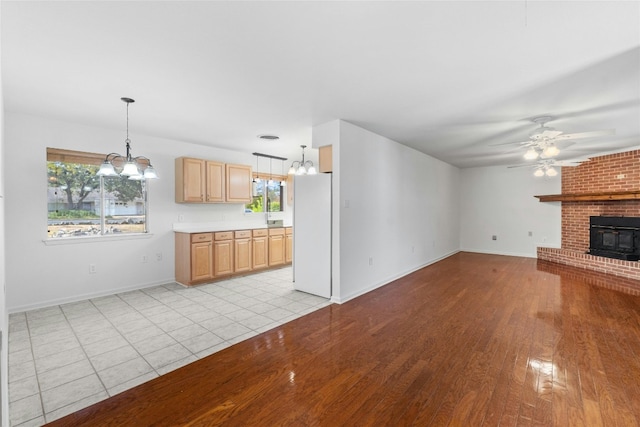 unfurnished living room with a wealth of natural light, ceiling fan with notable chandelier, and light hardwood / wood-style flooring