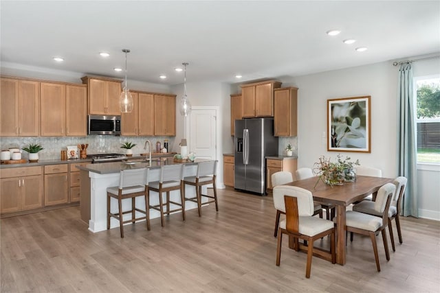 kitchen with tasteful backsplash, stainless steel appliances, decorative light fixtures, and a center island with sink