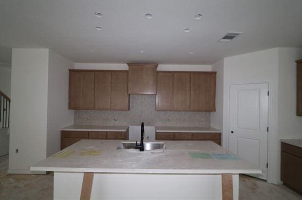 kitchen featuring tasteful backsplash, an island with sink, and sink